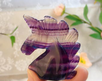 May include: A purple and white fluorite unicorn figurine. The unicorn is carved from a single piece of fluorite and has a detailed mane and horn.