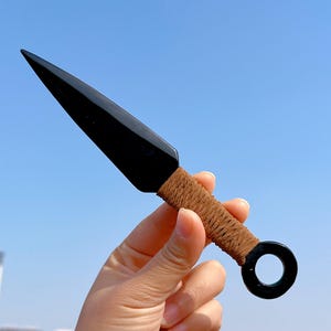 May include: Black throwing knife with a brown leather wrap and a black ring at the end of the handle.
