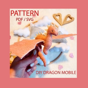 May include: DIY dragon mobile pattern in PDF and SVG format. The pattern includes a pink felt dragon with white felt spikes and wings. The dragon is hanging from a wooden hoop with clouds and hearts.