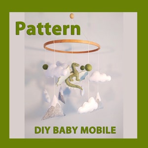 Puede incluir: Patrón de móvil de bebé DIY con un dragón de fieltro verde, nubes de fieltro blanco y montañas de fieltro gris. El móvil está suspendido de un anillo de madera.