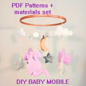 May include: DIY baby mobile kit with PDF patterns and materials. The mobile features a wooden ring, pink felt dragons, gray felt stars, white felt clouds, and a wooden crescent moon.