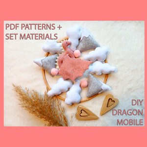 May include: A DIY dragon mobile kit with felt dragon, mountains, clouds, and wooden hearts. The mobile includes the text "PDF PATTERNS + SET MATERIALS" and "DIY DRAGON MOBILE". The dragon is pink, and the mountains are gray and white.