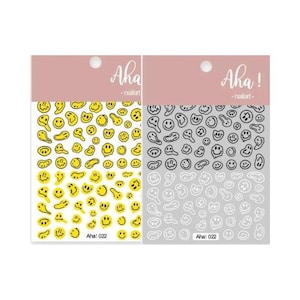May include: Two sheets of nail art stickers featuring a smiley face design. One sheet has yellow smiley faces with black outlines. The other sheet has black smiley faces with white outlines. Both sheets have the text "Aha! 022" printed on them.