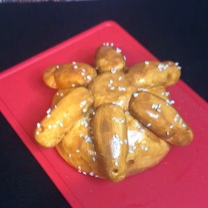 May include: A golden brown pastry with a star shape and white sesame seeds on top. The pastry is on a red surface.