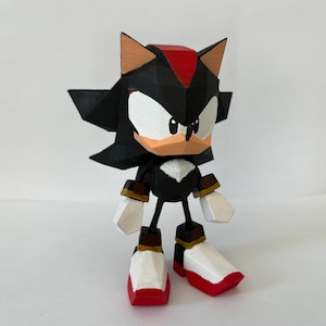 Peut inclure: Une figurine imprimée en 3D de Shadow the Hedgehog de la série de jeux vidéo Sonic the Hedgehog. La figurine est de style low-poly, avec un design simplifié.