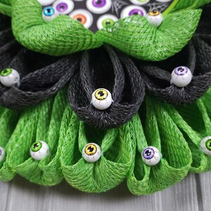 May include: A green and black Halloween wreath with a welcome sign and googly eyes.