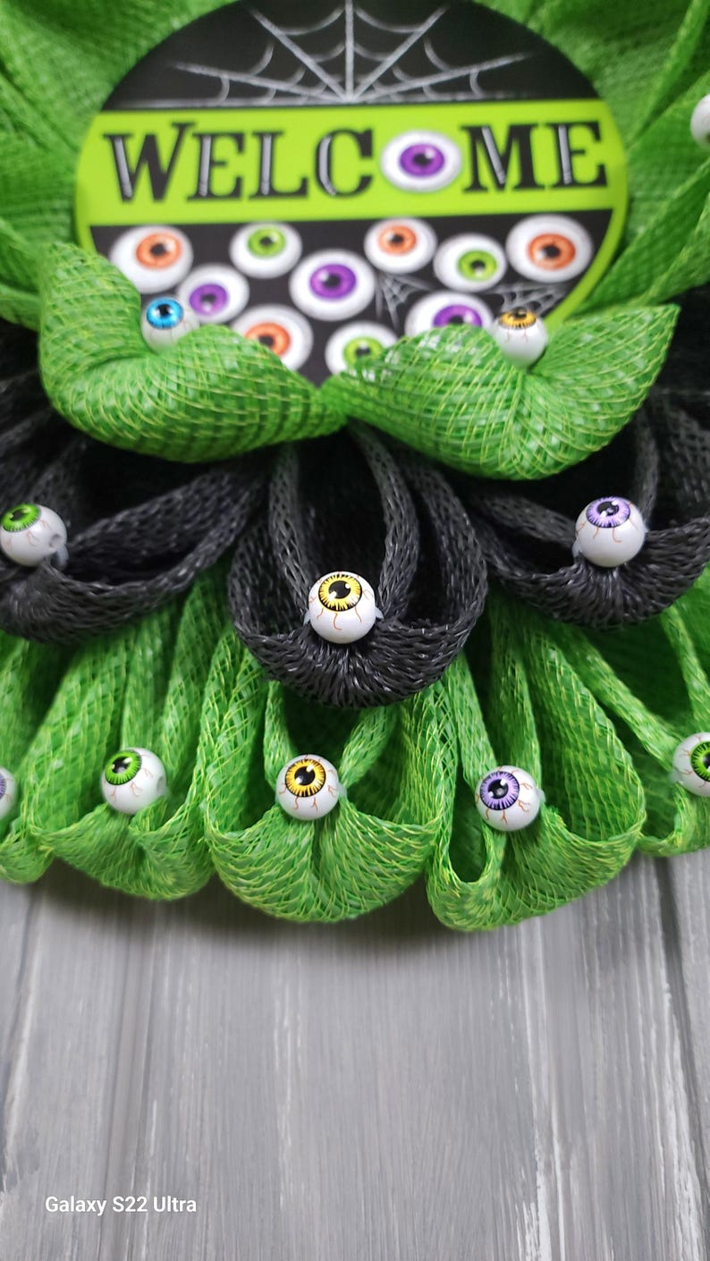 May include: A green and black Halloween wreath with a welcome sign and googly eyes.