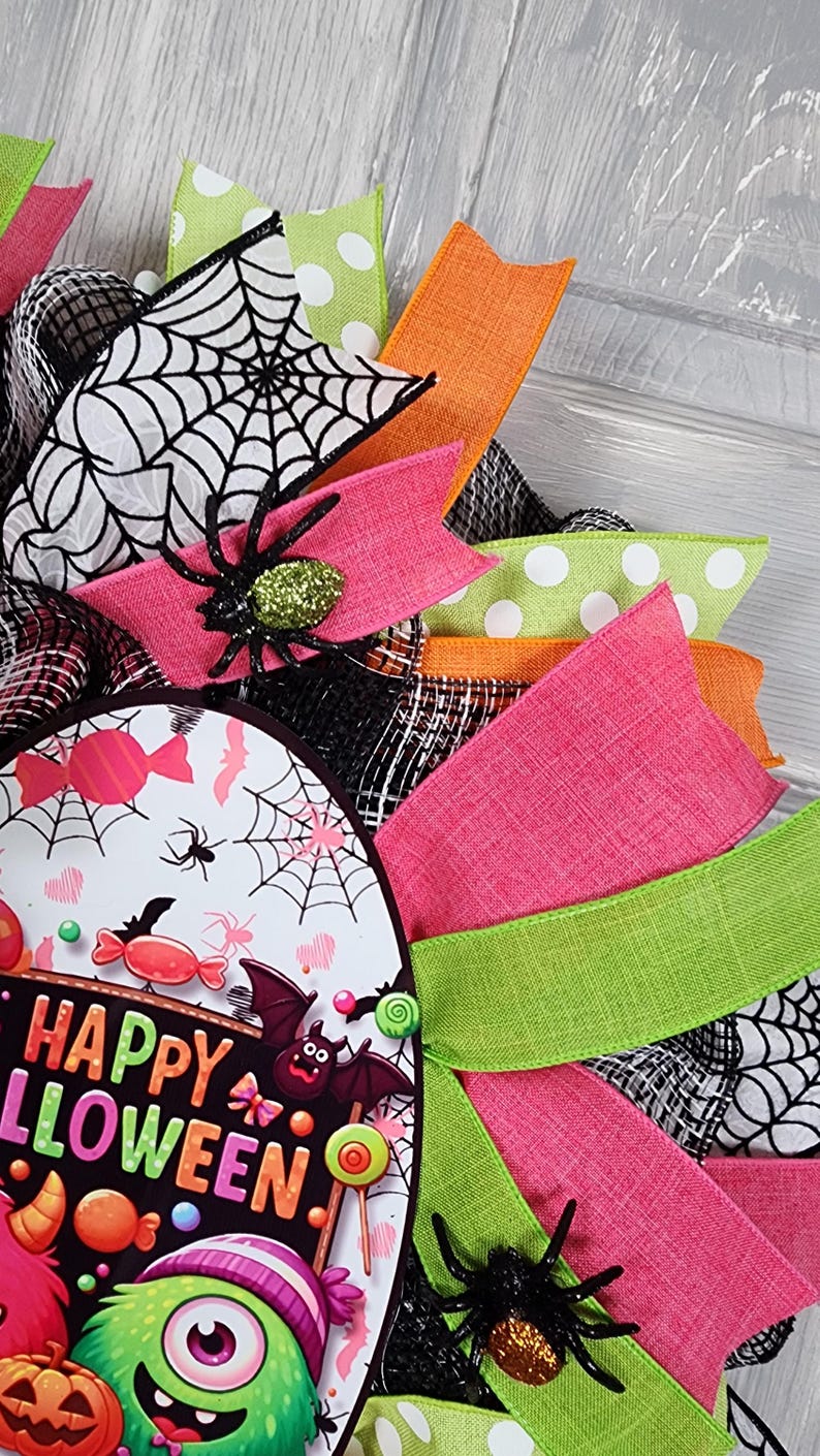 Puede incluir: Una colorida corona de Halloween con un dise&ntilde;o circular. La corona presenta cintas rosas, verdes, naranjas y blancas con lunares. Un letrero central dice "Happy Halloween" con monstruos de dibujos animados, ara&ntilde;as y caramelos.