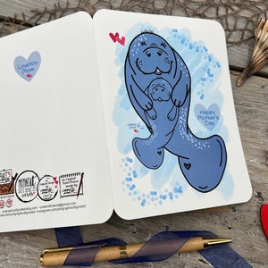 This picture shows the front and back of the card. A Mothers Day greeting card with a blue watercolor background and a illustration of two manatees. It also has bubbles all around, to show they are swimming. The larger momma manatee is holding the smaller manatee in her flippers. The card has the text Happy Mothers Day in a heart shape on the front. It has the text Love You Mom in a heart shape on the back of the card along with my logos.