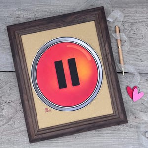 May include: A framed illustration of a red button with a silver border and a black pause symbol. The button is on a brown background.