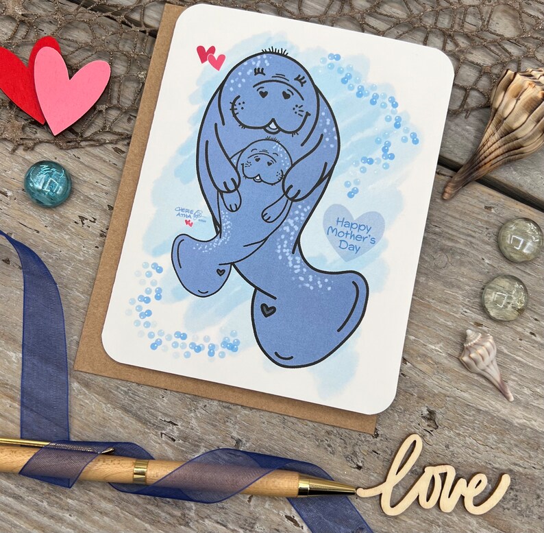 Printed on 80 lb white card stock this Mothers Day card has two original illustrated manatees that represents a momma and child. The larger manatee is holding the smaller manatee in its flippers. It has a blue digital watercolor background with bubbles to show them swimming in the ocean. The card has the text Happy Mothers Day along with my signature hearts.