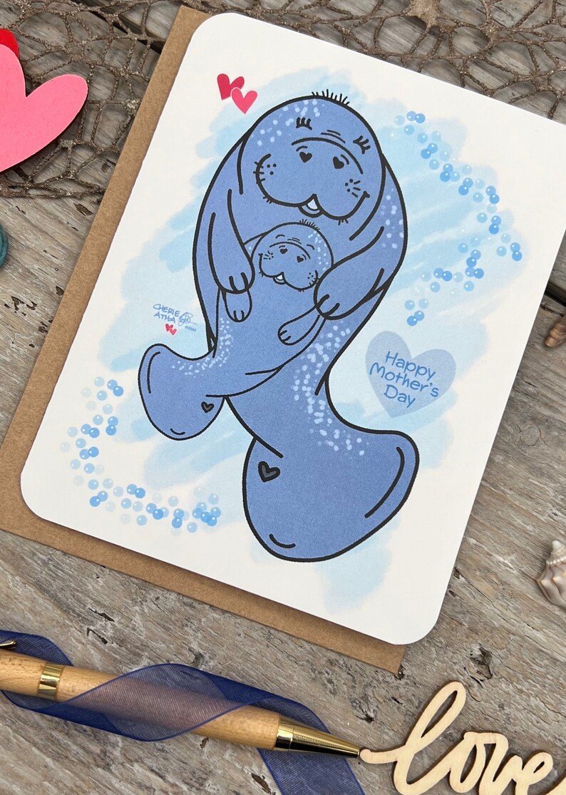 A Mothers Day greeting card with a blue digital watercolor background and a mother manatee and young manatee. The manatee is holding the baby manatee in its flippers. The card has the text Happy Mother's Day in a heart shape. It also includes my signature hearts.