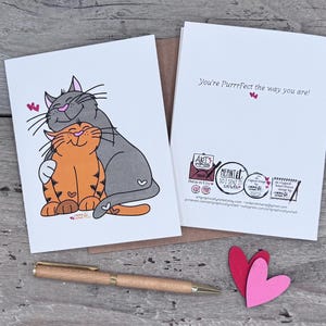 May include: A white greeting card featuring a cartoon illustration of a gray cat hugging an orange tabby cat with small pink hearts. The inside of the card displays the text "You're Purrfect the way you are!" along with various small logos and contact information.