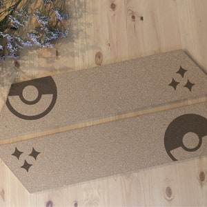 May include: Two cork coasters with a brown and white design. One coaster features a stylized Pokeball with a white circle and a white crescent moon. The other coaster features three white stars.