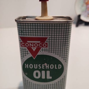 Może przedstawiać: Vintage metalowa puszka oleju domowego Conoco z czerwono-białym wylewką. Puszka ma zielono-biały wzór w kratkę z logo Conoco i napisem "Household Oil" w zielonym kółku.