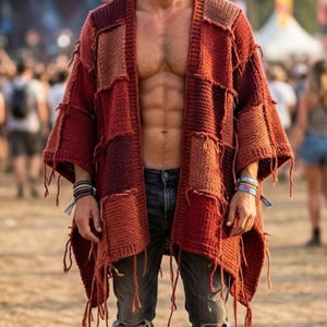 May include: A chunky knit patchwork cardigan in various shades of rust, terracotta, and deep red. The garment features an open front, wide sleeves, and frayed yarn edges throughout. It is paired with distressed charcoal gray denim jeans.