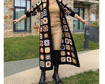 Könnte beinhalten: Langer, offener Häkel-Cardigan in Schwarz mit bunten quadratischen Motiven. Die Quadrate sind in Creme-, Gelb-, Braun- und Burgundertönen gehalten. Der Cardigan hat lange Ärmel und einen knielangen Saum.