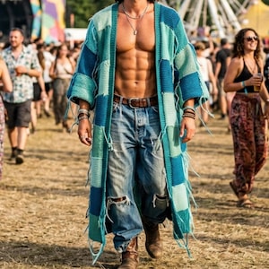 May include: A person wearing a patchwork cardigan in shades of teal and blue, paired with ripped blue jeans and brown boots. The cardigan has a fringed hem. The background shows a festival setting with a Ferris wheel.