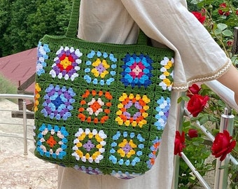 May include: A handmade crochet tote bag featuring a vibrant granny square pattern in multiple colors including yellow, orange, blue, purple, and white, all joined together with a dark green yarn border and matching green shoulder straps.