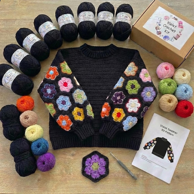 May include: A black sweater with colorful floral crochet sleeves, surrounded by black yarn balls, a crochet hook, and a "Violet Crochet Kit" box. Additional colorful yarn balls and a pattern sheet are also present, creating a craft-themed arrangement.