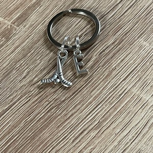 May include: Silver keyring with a hockey stick charm and a letter E charm.