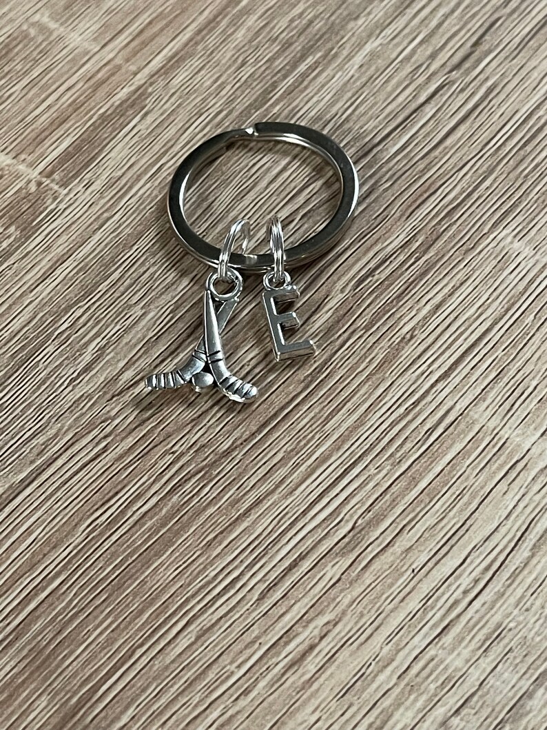 May include: Silver keyring with a hockey stick charm and a letter E charm.