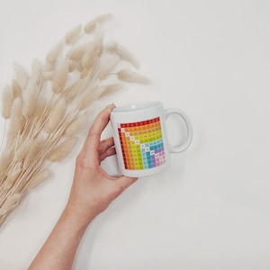 Könnte beinhalten: Eine weiße Keramiktasse mit einem darauf gedruckten Regenbogen-Multiplikationstableau. Die Tasse hat einen Henkel auf der rechten Seite.