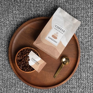 Puede incluir: Vista superior de una bandeja de madera con art&iacute;culos relacionados con el caf&eacute;. Una bolsa de caf&eacute; espresso y un paquete peque&ntilde;o est&aacute;n en la bandeja, junto con un peque&ntilde;o cuenco de madera lleno de granos de caf&eacute; y una cuchara dorada. El texto "COFFEE Espresso" es visible.
