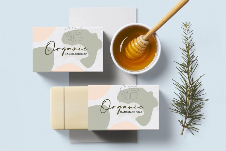 Puede incluir: Dos cajas blancas con un dise&ntilde;o abstracto verde y rosa y el texto "Organic Handmade Soap". Las cajas est&aacute;n sobre una superficie azul claro con una peque&ntilde;a rama de hojas verdes y un cuenco de miel con un cuchar&oacute;n de miel.