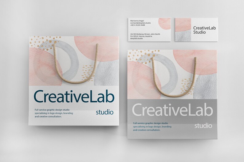 Op de afbeelding: Twee witte boodschappentassen met een bruin touwhandvat. De tassen hebben een aquarelontwerp met roze, grijze en gouden cirkels. De tekst "CreativeLab studio" is op de tassen gedrukt.