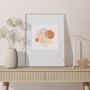 Puede incluir: Una impresi&oacute;n art&iacute;stica abstracta enmarcada con formas y l&iacute;neas en tonos tierra se encuentra sobre una consola de madera clara. Un jarr&oacute;n beige con flores secas, una vela y una concha decorativa completan la decoraci&oacute;n minimalista.