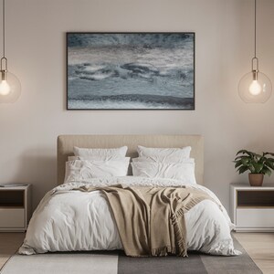 Op de afbeelding: Een wit bed met een bruin dekbed en witte kussens in een slaapkamer met twee nachtkastjes en twee hangende globe lampen. Een ingelijst abstract schilderij hangt boven het bed.