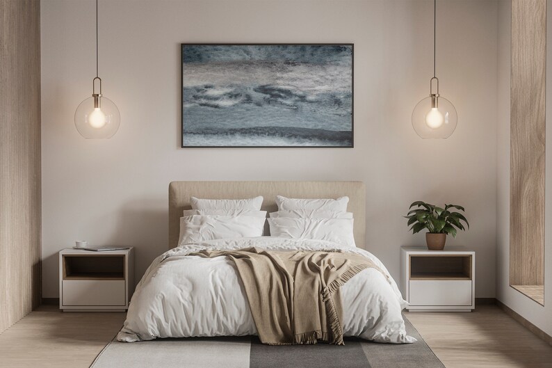Op de afbeelding: Een wit bed met een bruin dekbed en witte kussens in een slaapkamer met twee nachtkastjes en twee hangende globe lampen. Een ingelijst abstract schilderij hangt boven het bed.