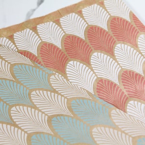 K&ouml;nnte beinhalten: Zwei Bl&auml;tter braunes Geschenkpapier mit einem wei&szlig;en und blauen geometrischen Muster auf einem Blatt und einem wei&szlig;en und korallenfarbenen geometrischen Muster auf dem anderen Blatt.