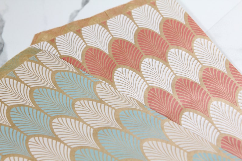 K&ouml;nnte beinhalten: Zwei Bl&auml;tter braunes Geschenkpapier mit einem wei&szlig;en und blauen geometrischen Muster auf einem Blatt und einem wei&szlig;en und korallenfarbenen geometrischen Muster auf dem anderen Blatt.