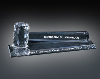 May include: A clear crystal desk set with a gavel-shaped paperweight and a rectangular nameplate. The nameplate reads "GORDON MCKENNAN Merit Investment Corp. - President/CEO".