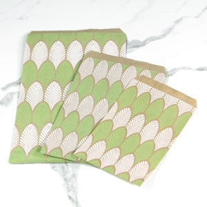 May include: Three brown paper gift bags with a green and white leaf pattern. The bags are nested inside each other, with the largest bag at the bottom and the smallest bag at the top.
