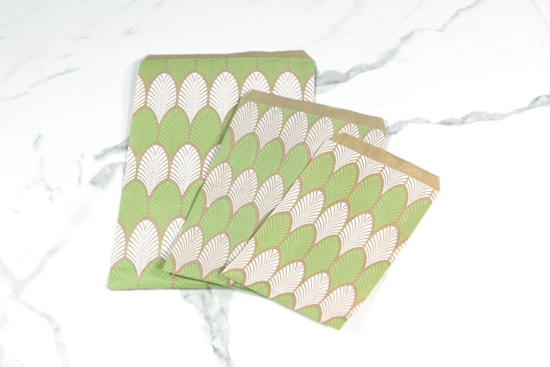 May include: Three brown paper gift bags with a green and white leaf pattern. The bags are nested inside each other, with the largest bag at the bottom and the smallest bag at the top.