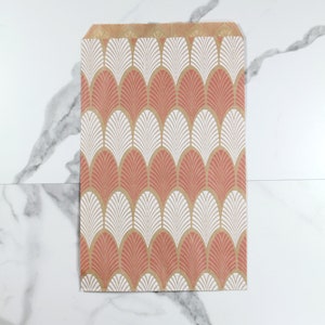 K&ouml;nnte beinhalten: Eine braune Papiert&uuml;te mit einem geometrischen Muster in Rosa und Wei&szlig;. Das Muster zeigt ein sich wiederholendes Design aus stilisierten Bl&auml;ttern.