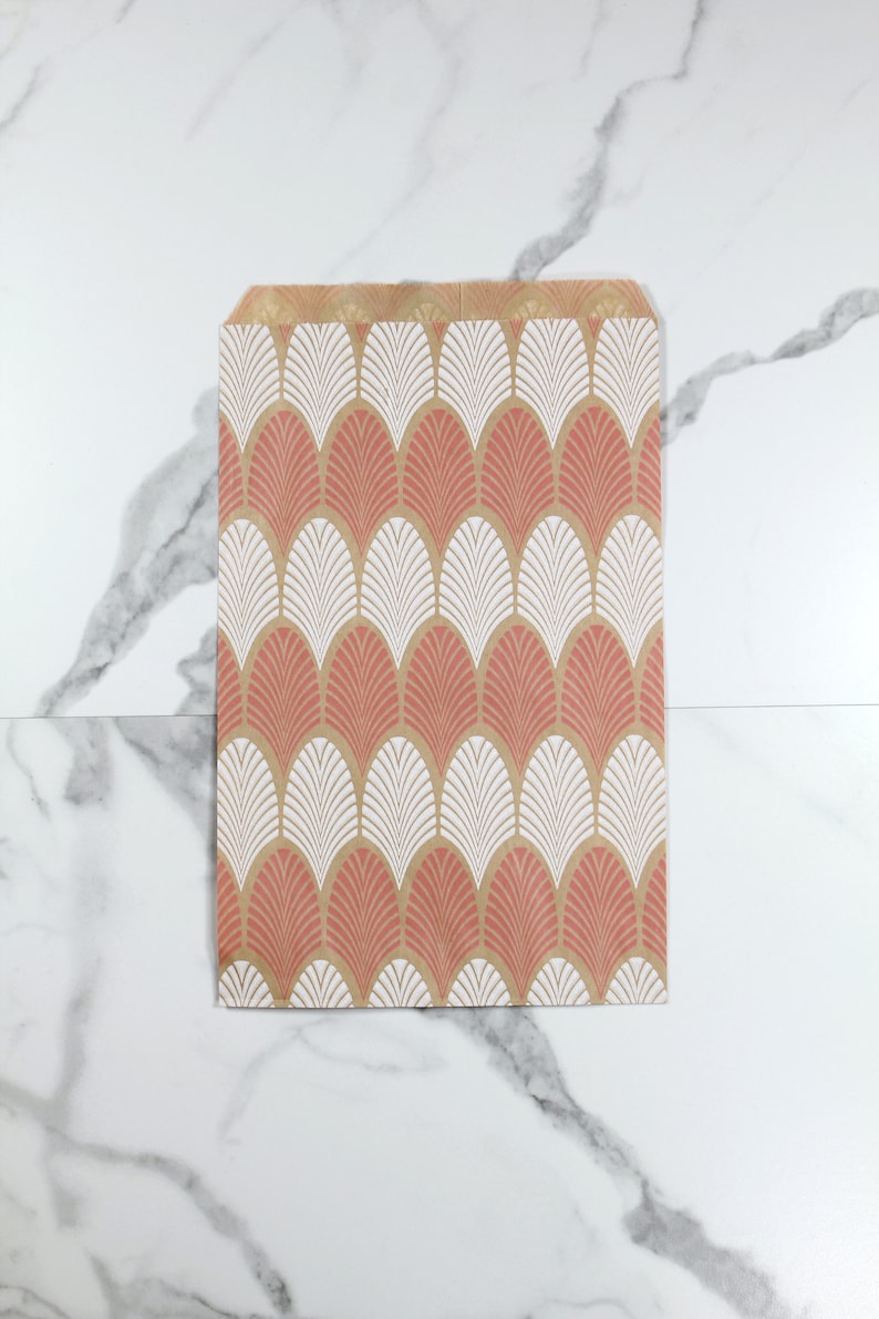 K&ouml;nnte beinhalten: Eine braune Papiert&uuml;te mit einem geometrischen Muster in Rosa und Wei&szlig;. Das Muster zeigt ein sich wiederholendes Design aus stilisierten Bl&auml;ttern.