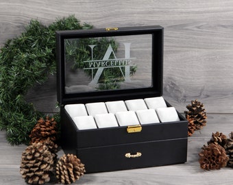 May include: Black leather watch box with a glass top and a drawer. The box has 12 compartments for watches and is engraved with the initials "JA" and the name "WYKSEPTI2".