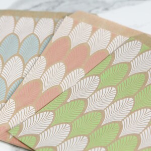 May include: Three brown paper gift bags with a white and coloured leaf pattern. The bags are stacked on top of each other, with the green bag on the bottom, the pink bag in the middle, and the blue bag on top.