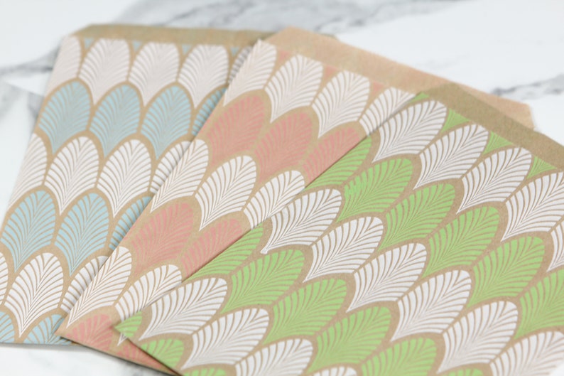 May include: Three brown paper gift bags with a white and coloured leaf pattern. The bags are stacked on top of each other, with the green bag on the bottom, the pink bag in the middle, and the blue bag on top.