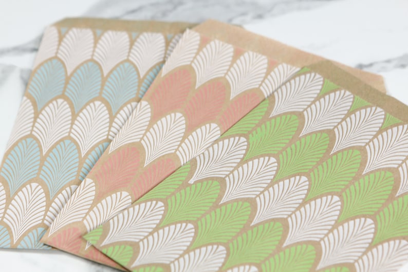 K&ouml;nnte beinhalten: Drei braune Papiert&uuml;ten mit einem wei&szlig;en und farbigen Blatt-Muster. Die Taschen sind in den Farben Blau, Rosa und Gr&uuml;n.