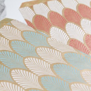 K&ouml;nnte beinhalten: Zwei Bl&auml;tter braunes Geschenkpapier mit einem wei&szlig;en und blauen geometrischen Muster. Das Muster ist ein sich wiederholendes Design aus stilisierten Federn.