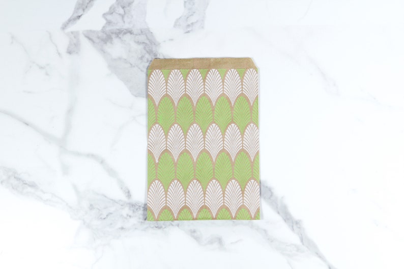 K&ouml;nnte beinhalten: Eine braune Papiert&uuml;te mit einem geometrischen Muster in Gr&uuml;n und Wei&szlig;. Das Muster zeigt ein sich wiederholendes Design aus stilisierten Bl&auml;ttern.