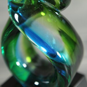 May include: A glass award with a swirling design in shades of green and blue. The award is on a black base.