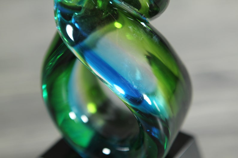 May include: A glass award with a swirling design in shades of green and blue. The award is on a black base.