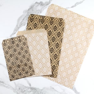 May include: Four brown paper bags with a black and white damask pattern. The bags are different sizes and are arranged in a row on a white marble surface.