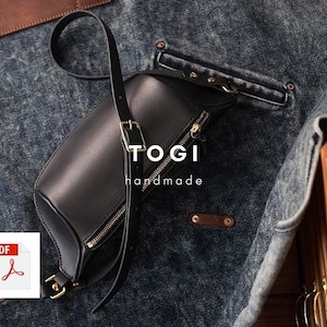 May include: A black leather crossbody bag with a gold zipper and a gold buckle. The bag is on a denim background and has the text "TOGI handmade" on it.